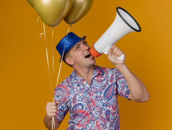 橙色快乐的年轻人戴着蓝色的帽子拿着气球在橙色的喇叭上讲话说话派对蓝色