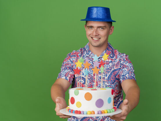 派对带着微笑的年轻人戴着蓝色的帽子拿着蛋糕孤立在绿色蛋糕帽子戴着