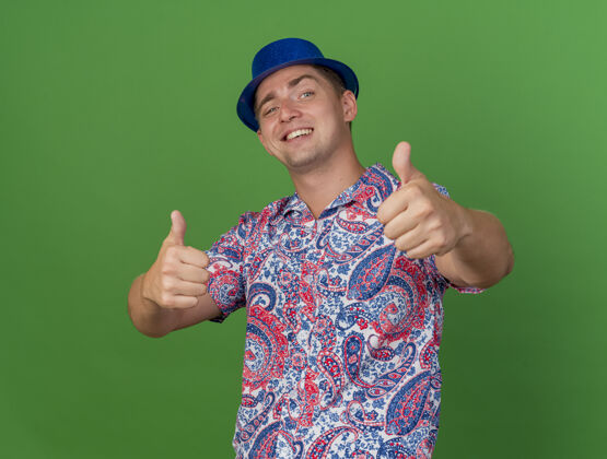 年轻戴着蓝色帽子的年轻人微笑着 在绿色的草坪上竖起大拇指拇指绿色秀