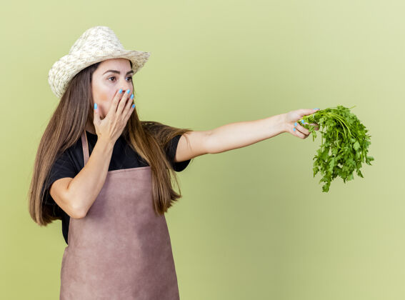 花园一个穿着制服的漂亮的园丁女孩戴着园艺帽 一边伸出香菜 一边用橄榄绿的手捂住嘴巴盖园艺绿色