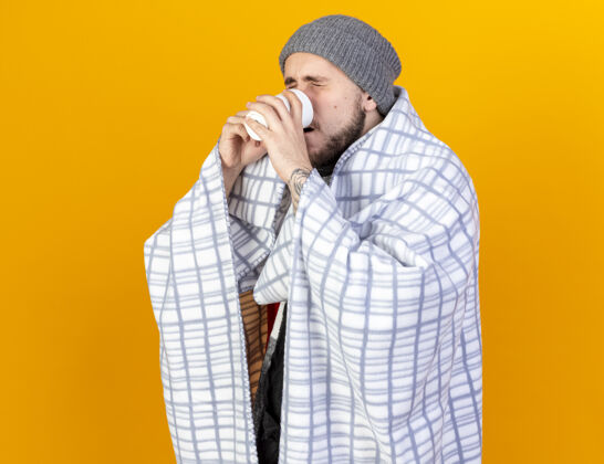 年轻人一个戴着冬日帽 披着方格围巾 喝着隔离在橘色墙上的茶的年轻人人包裹表情