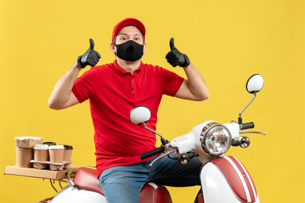 摩托车俯视图：自信的快递员身穿红色上衣 戴着帽子手套 戴着医用口罩 坐在滑板车上传递订单 动作正常手套命令摩托车
