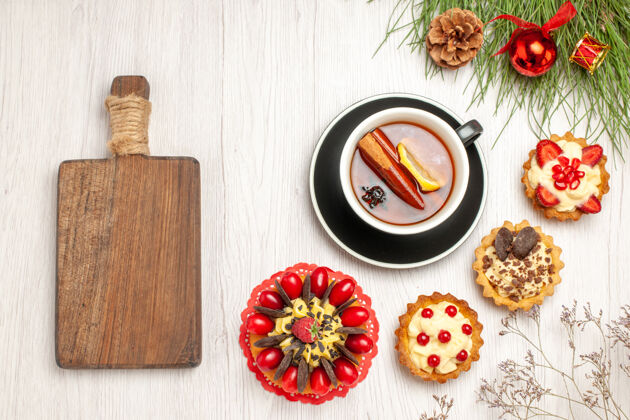 胡椒粉俯瞰一杯柠檬肉桂茶浆果蛋糕馅饼和松树叶子 白色木质地面上有圣诞玩具和砧板圣诞蛋糕木板