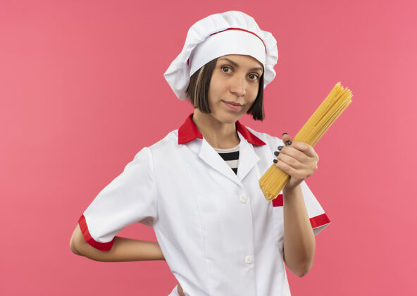 背部身着厨师制服的年轻女厨师手拿意大利面 手放在粉红色的墙上 手背孤立着意大利面人表情