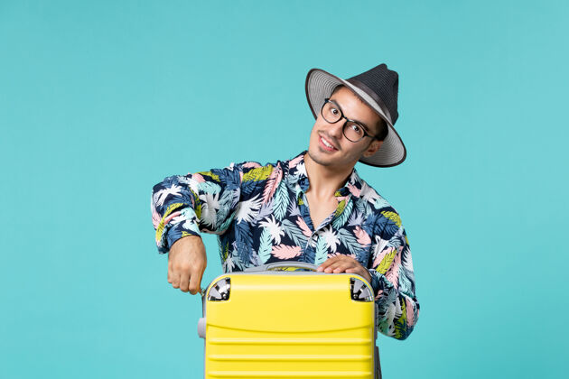 微笑年轻男子正拿着他的黄色袋子准备在蓝色的墙上旅行旅行快乐年轻男性