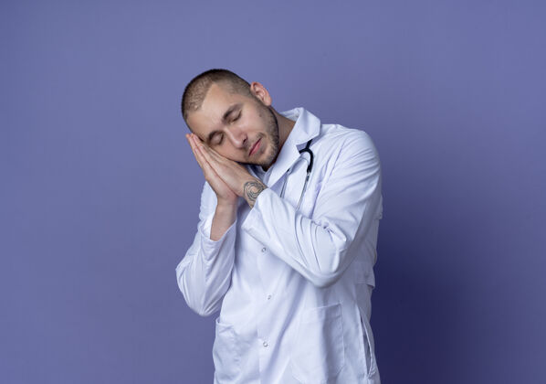 穿着昏昏欲睡的年轻男医生 穿着医用长袍 戴着听诊器 闭着眼睛在紫色的墙上做着睡觉的姿势医生长袍表情