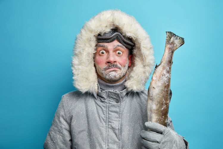 拼图在严寒的天气里 一个被冻住的男人穿着灰色的冬衣 戴着手套 抱着鱼 戴着滑雪眼镜 在户外呆了很长时间断绝男人爱好