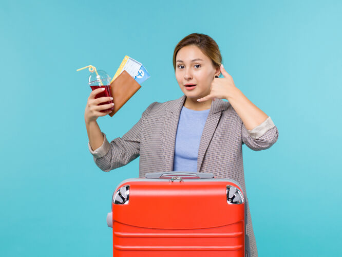 果汁正面图：度假中的女性拿着一杯新鲜的果汁和机票坐在蓝色的办公桌上旅行飞机度假海上旅行假期成人旅行