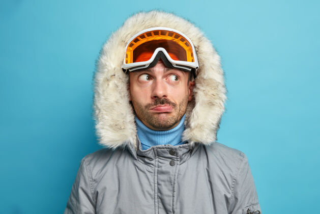 运动男徒步旅行者一边若有所思地看着一边 一边戴着滑雪护目镜和带兜帽的冬季夹克 一边在假期里积极休息 一边享受喜爱的运动穿着白种人成人