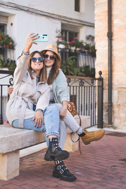朋友时尚女性朋友坐在街上的长椅上自拍友谊时尚长凳