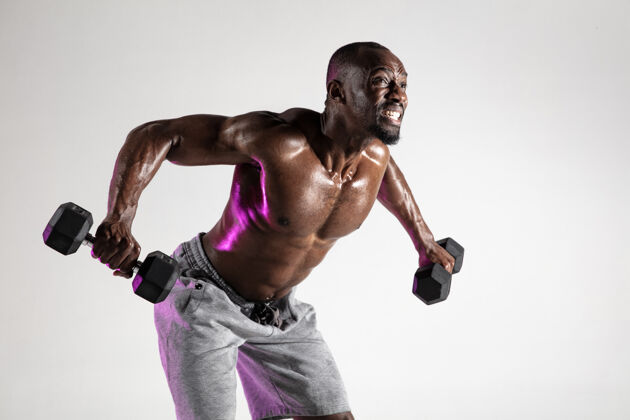 运动因此 成长的翅膀年轻的非洲裔美国健美运动员灰色背景下的培训肌肉单一的男模在运动服与重量概念的运动 健美 健康的生活方式交叉赤膊非洲