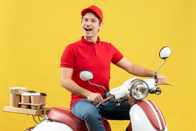 摩托车俯视图：微笑的年轻人穿着红色上衣 戴着帽子 坐在黄色墙上的滑板车上传递命令微笑传送带滑板车