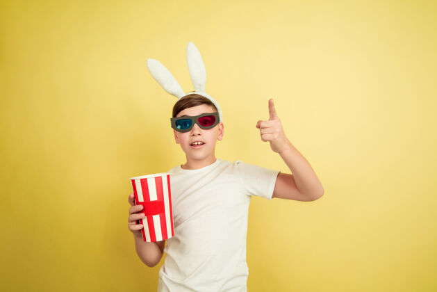 自信戴着爆米花的眼镜看电影白人男孩在黄色背景上扮演复活节兔子复活节快乐美丽的男模人类情感的概念 面部表情 节日复制空间男性潮流庆祝