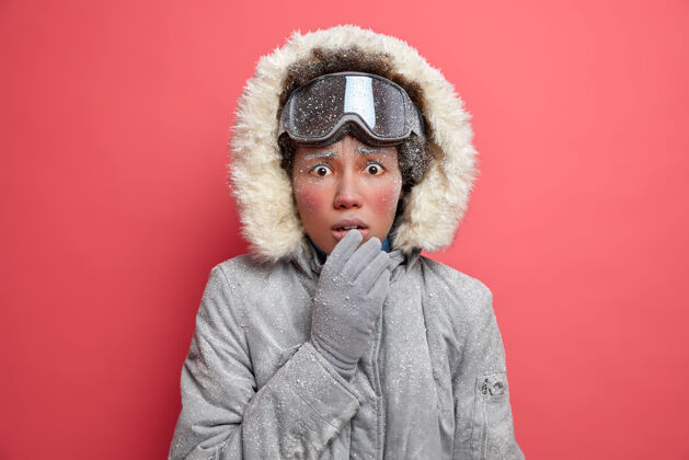 冰冻迷惑不解的冻僵女人 红着冰冷的脸 看起来很尴尬 冻得浑身发抖 戴着滑雪镜 灰色外套 在暴风雪天气里徒步旅行外套风格冰冻