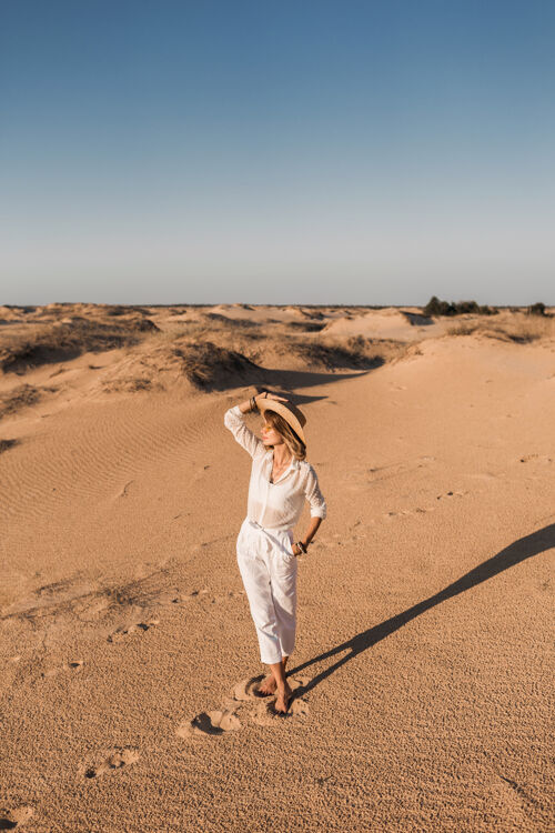 年轻一个穿着白色衣服 戴着草帽 在沙漠沙滩上行走的时尚美女模特波西米亚冒险
