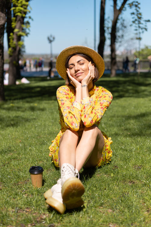 户外穿着黄色夏装戴着帽子坐在公园草地上的女人的户外肖像自然年轻街道