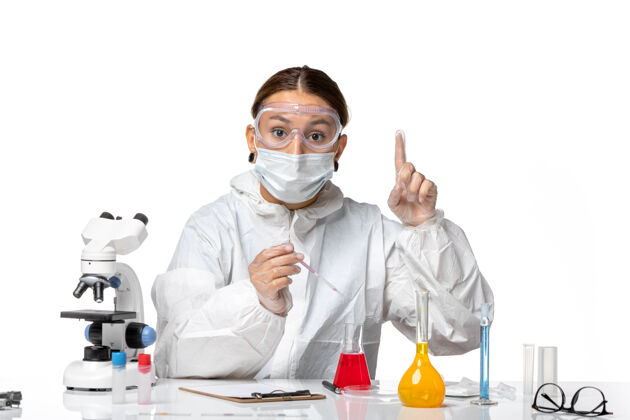 实验室外套前视图穿着防护服 戴着面罩的女医生正在用浅白色背景的冠状病毒大流行病毒冠状病毒溶液工作面罩专业医院