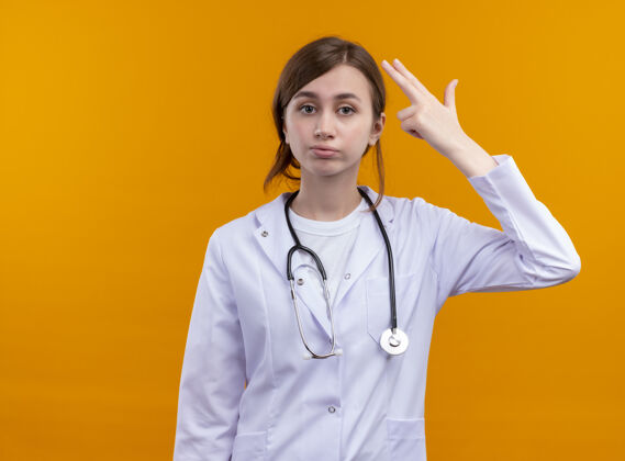 女性厌倦了年轻的女医生穿着医用长袍和听诊器在孤立的橙色空间里做的手势橙色医疗太空