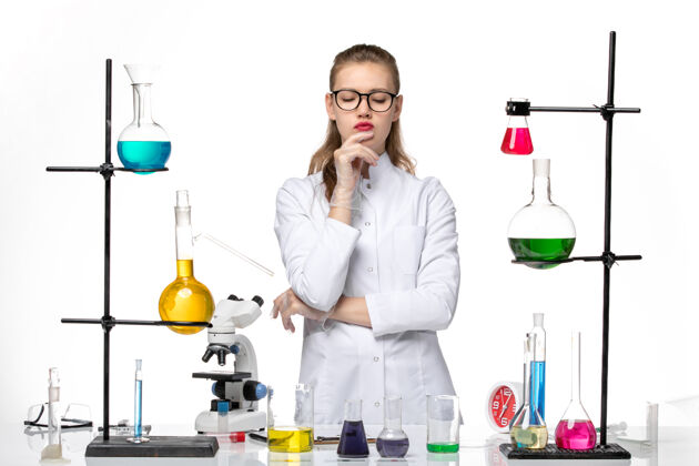 不同前视图穿着医疗服的女化学家在用不同的解决方案工作 并思考白色背景化学大流行的冠状病毒人白人思维