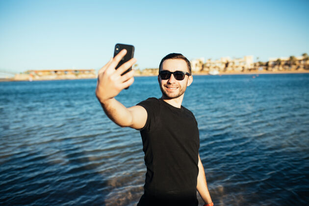 电话年轻帅哥在沙滩上用智能手机自拍自然肖像一个