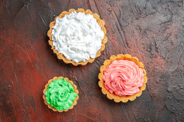 深色顶视图不同大小的小馅饼与绿色 粉红色和白色糕点奶油深红色的表面花帽子花束
