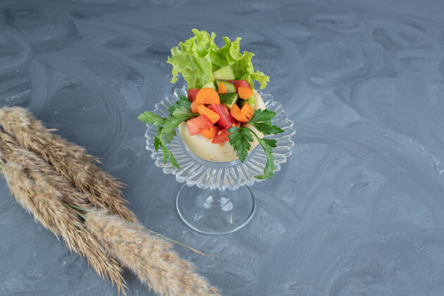 美味一小块切碎的蔬菜放在玻璃基座上的白萝卜上 大理石桌上放着针叶草茎可口黄瓜美味