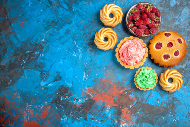 花束覆盆子蛋糕 小馅饼 饼干和蓝粉色表面覆盆子碗的俯视图小浪漫花