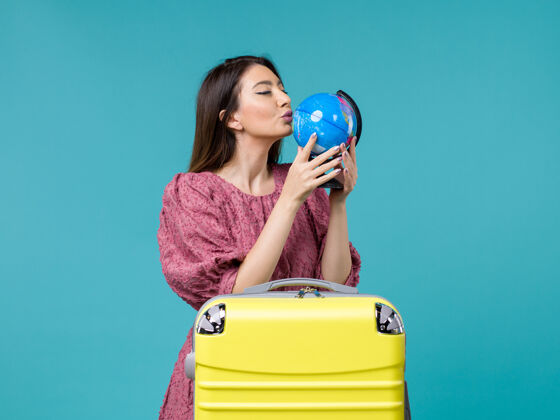 人前视女性在旅行中拿着地球仪在蓝色的背景上旅行旅行旅行旅行旅行旅行旅行女人海前面成人微笑