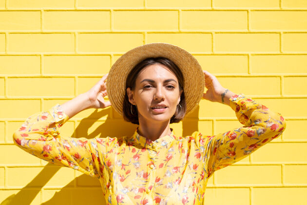 太阳黄砖墙上戴着黄色夏装和帽子的女人冷静而积极街道酷明亮