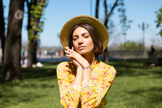 人穿着黄色夏装戴着帽子坐在公园草地上的户外时尚写真欢乐街道肖像