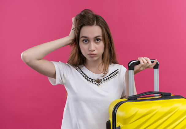 自信自信的年轻旅行家女孩拿着手提箱 把手放在孤立的粉红色空间头上粉色女孩手提箱