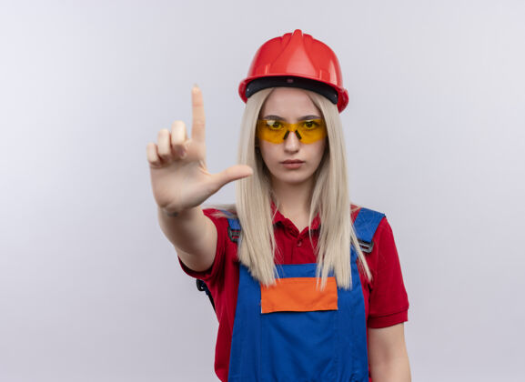 空间自信的年轻金发工程师建筑工女孩穿着制服 戴着安全眼镜 在隔离的空白处展示般的 还有复印空间制服年轻人工程师