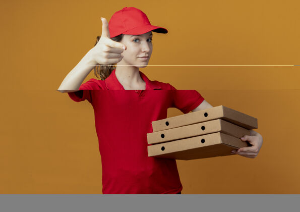 背景自信的年轻漂亮的送货女孩 穿着红色制服 戴着帽子 手里拿着披萨包 对着橙色背景上孤立的摄像机做着手势手势女孩年轻