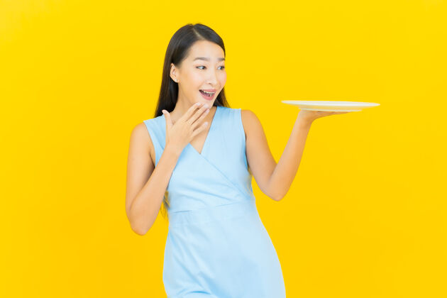 陶瓷画像美丽的亚洲年轻女子微笑着在黄色墙上的空盘子泰国面包师快乐