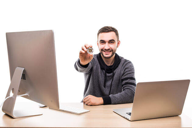 电脑一位面带微笑的企业家坐在办公桌旁 手持比特币 笔记本电脑和电脑隔着白色屏幕货币人比特币