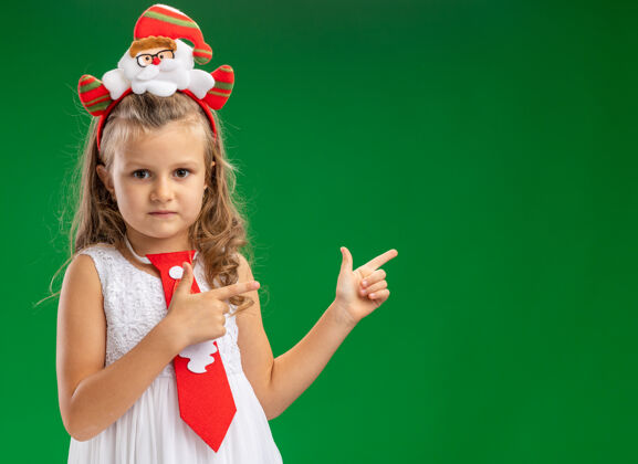 女孩看着镜头 小女孩戴着圣诞发箍 后面系着领带 背景是绿色的小圣诞节点