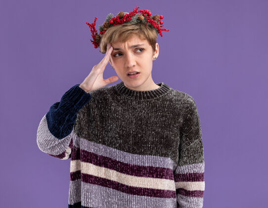 头迷茫的年轻漂亮女孩戴着圣诞花环望着侧面抚摸着孤立在紫色背景上的头圣诞节触摸紫色