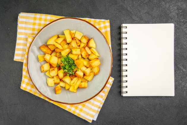记事本在深灰色的表面上有记事本的盘子里美味的炸土豆的俯视图晚餐农产品蔬菜