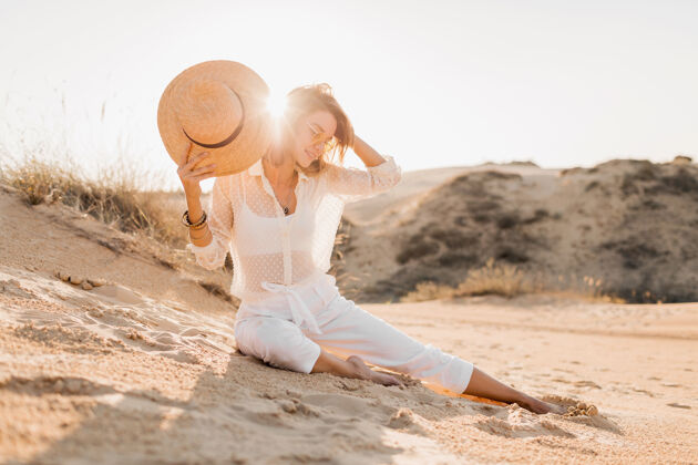 波西米亚穿着白色套装 戴着草帽的沙漠沙滩上的时髦美女休闲热模特