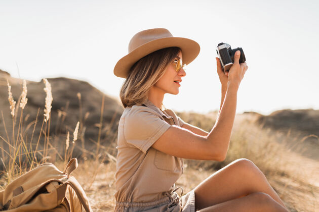 夏天沙漠中穿着卡其色长裙的迷人时尚年轻女子 在非洲旅行 戴着帽子和背包 用老式相机拍照配件游客摄影师