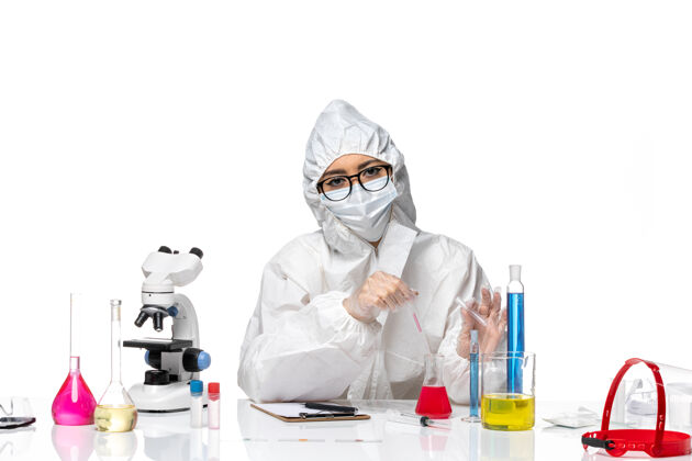 面罩前视图穿着特殊防护服的女化学家正在处理白色办公桌上的健康病毒化学溶液实验室套装药品