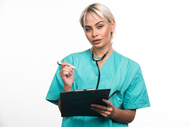 成人女医生用白墙上的钢笔在剪贴板上写东西站着文件夹拿着