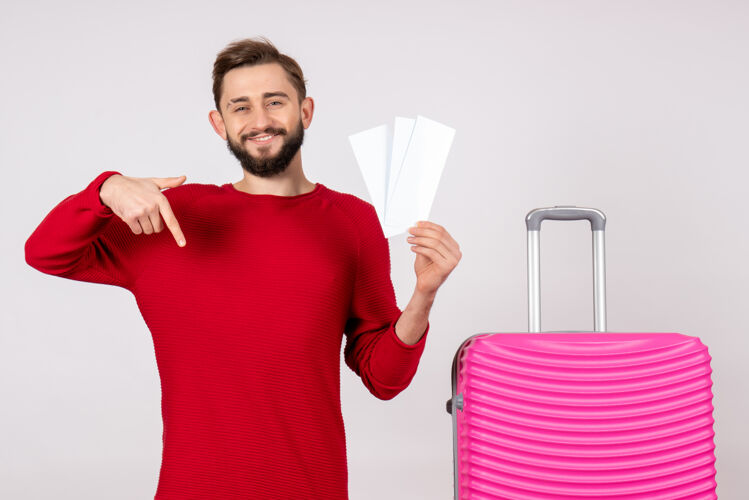游客正面图：年轻男性 手拿粉色包 手持机票 在白墙上航行 飞行 彩色旅行 旅游度假的情感照片风景机票航班