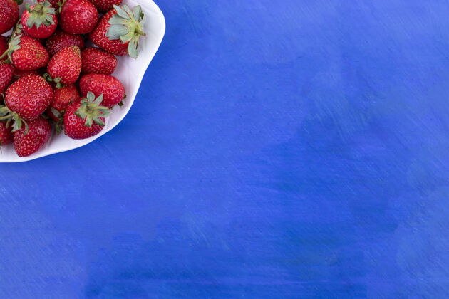 多在蓝色的表面上放满草莓的白色盘子刷新健康有机草莓