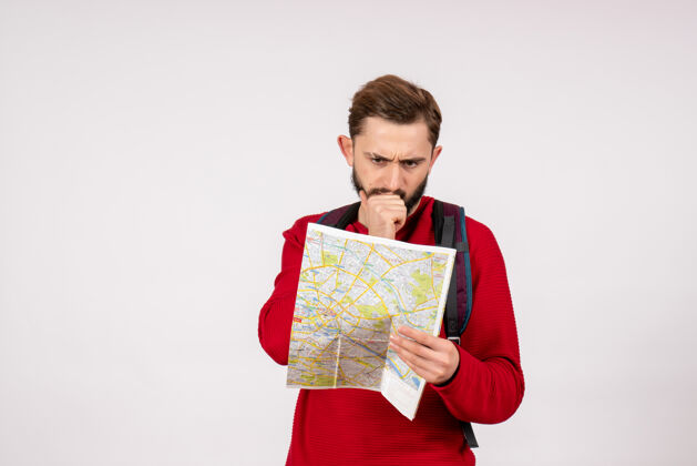 游客正面图年轻男性游客背着背包在白墙飞机上探索地图城市度假情感色彩旅游路线男人微笑路线