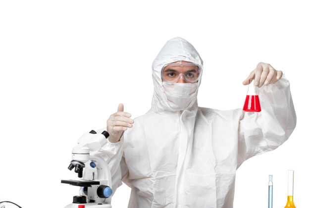 视图正面图：男医生穿着防护服 戴着面罩 因为在浅白的空间里有一个装有红色溶液的瓶子套装医疗实验室外套