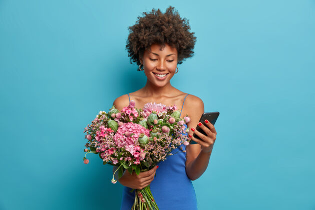 手机快乐微笑的女人看着智能手机展台笑容满面 手里拿着手机和一束鲜花情绪束满意