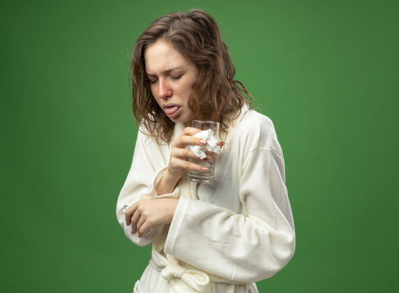 长袍咳嗽的年轻病女孩闭着眼睛穿着白色长袍拿着一杯水隔离在绿色水年轻穿