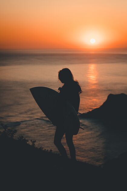 日出落日时分 一位孤独的女性手持冲浪板在海边散步水日落娱乐