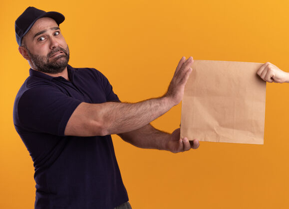 顾客穿着制服 戴着帽子的中年送货员把纸食品包装交给隔离在黄色墙上的客户中年关心给予